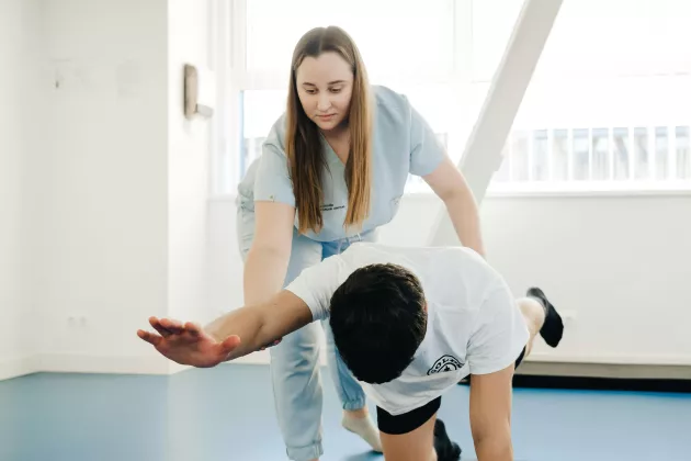 A healthcare worker who is teaching another person who's standing on his knees and hands, how to do exercises
